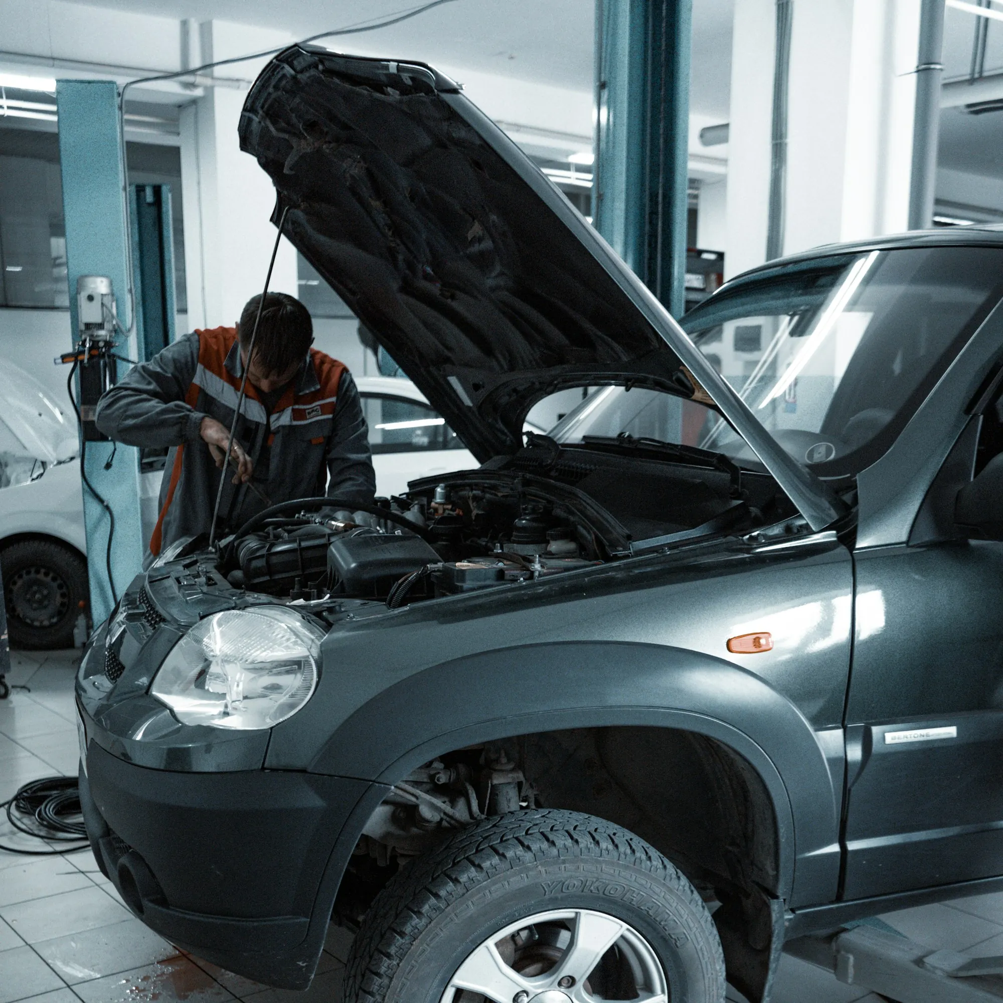 Mechanic working under the raised hood of a grey SUV